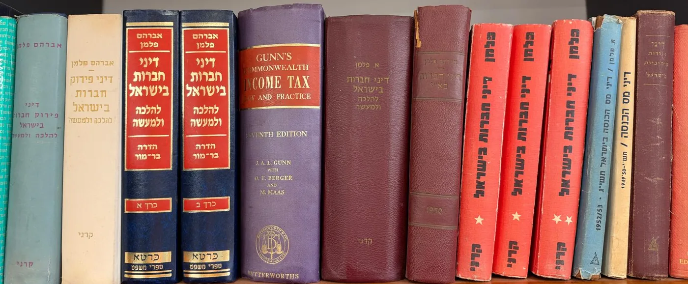 ספריו של אברהם פלמן על מדף במשרד: דיני חברות בישראל בשני כרכים, דיני פירוק חברות בישראל, דיני מס הכנסה בישראל ועוד